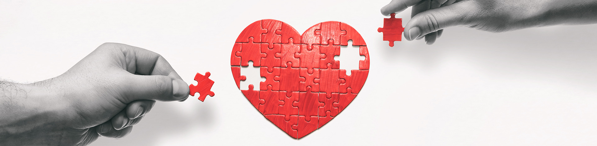 Hands holding puzzle pieces reach to complete a heart puzzle.